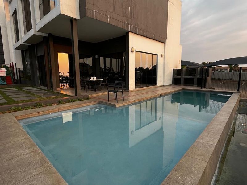 Modern apartment exterior featuring a private swimming pool, paved patio area, and a built-in outdoor braai facility.