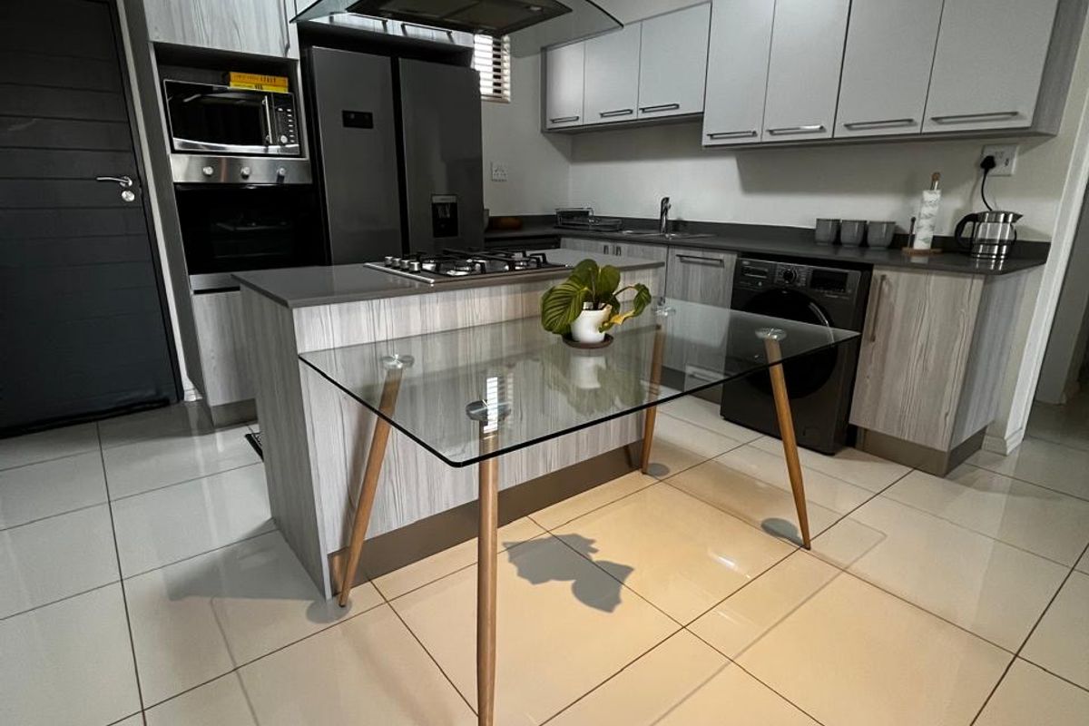 Modern kitchen featuring light wood-grain cabinetry, stone countertops, integrated appliances including a gas hob, extractor fan, and built-in oven with tiled flooring.