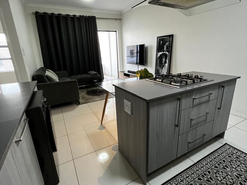 Modern open-plan living area featuring a kitchen island with a gas hob, extractor fan, and sleek cabinetry, seamlessly flowing into the lounge space.