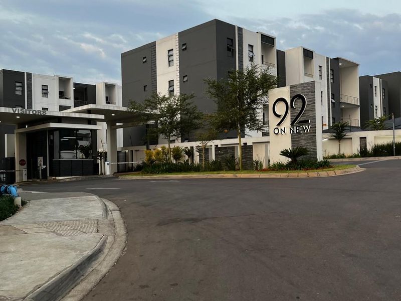The entrance to 92 on New apartment complex, featuring a modern security gatehouse, paved driveway, and contemporary multi-story residential building architecture.