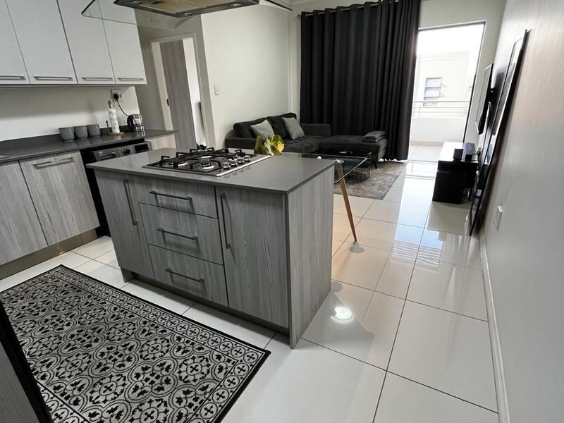 Modern open-plan living area featuring a kitchen island with gas hob, sleek cabinetry, tiled flooring, and direct access to a balcony.