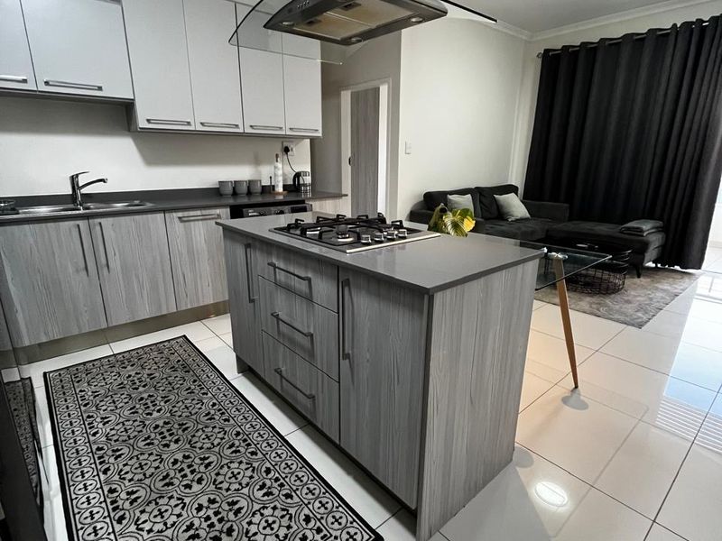 Modern open-plan kitchen featuring a central island with a gas hob, sleek cabinetry, and tiled flooring, seamlessly flowing into the living area.