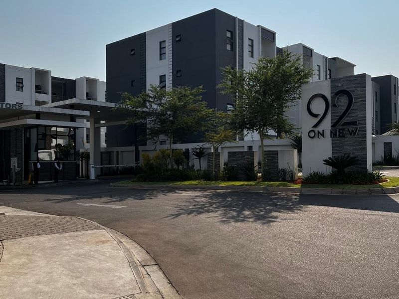 The entrance to 92 on New apartment complex, featuring a modern security gatehouse, paved driveway, and well-maintained landscaped grounds.