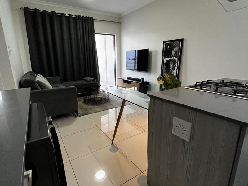 Modern open-plan living area featuring tiled floors, a compact kitchen with gas hob and extractor, and direct access to a balcony.
