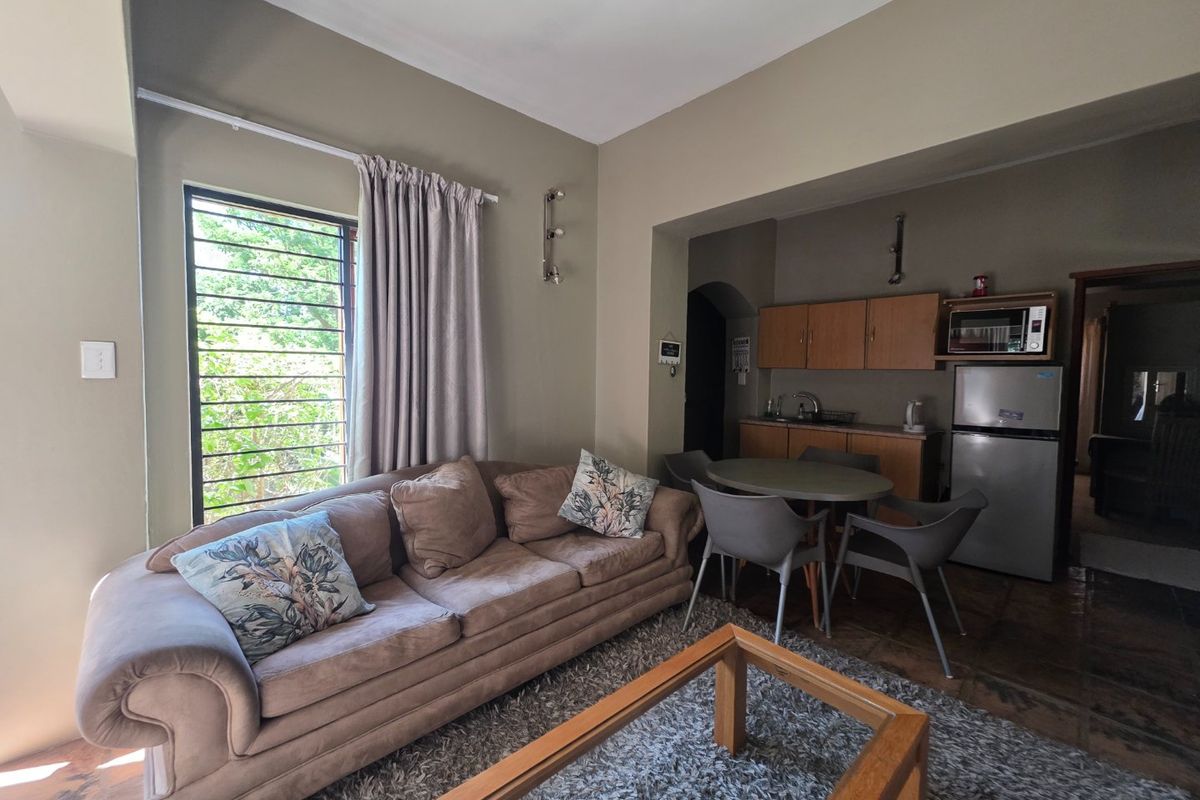 Open-plan living and kitchen area featuring tiled flooring, built-in cabinetry, and a window with security bars.
