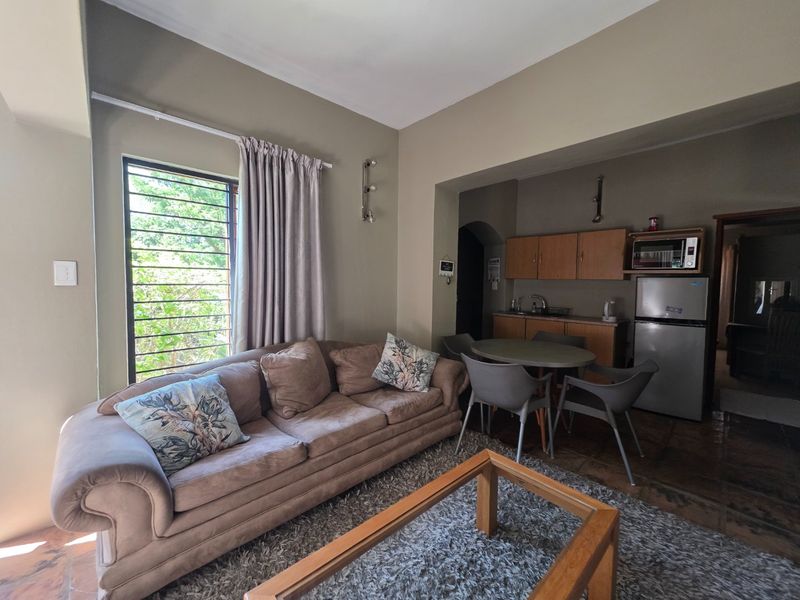 Open-plan living and kitchen area featuring tiled flooring, built-in cabinetry, and a window with security bars.