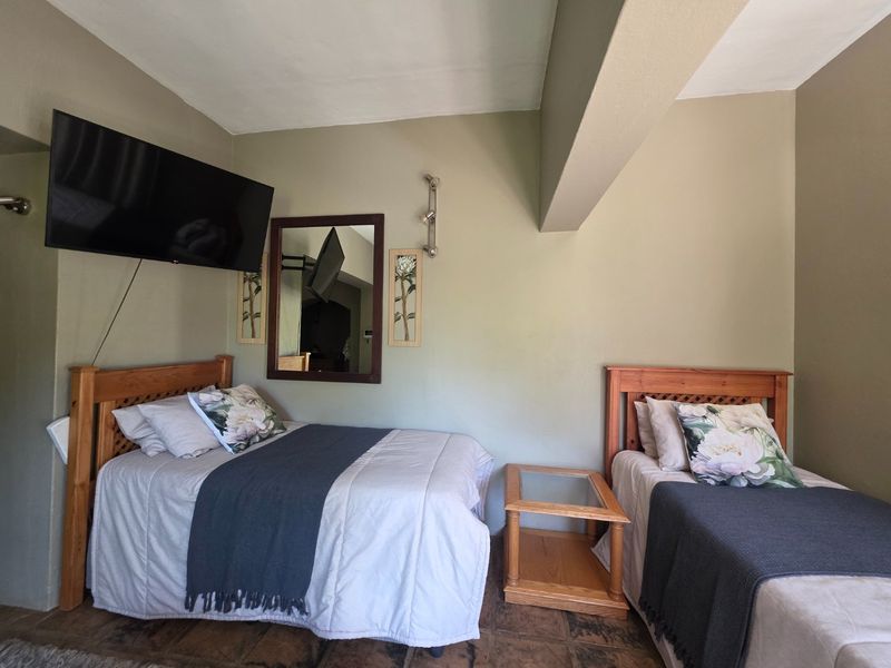 A bedroom featuring tiled flooring, a wall-mounted television, and a structural ceiling beam, providing a functional sleeping space.