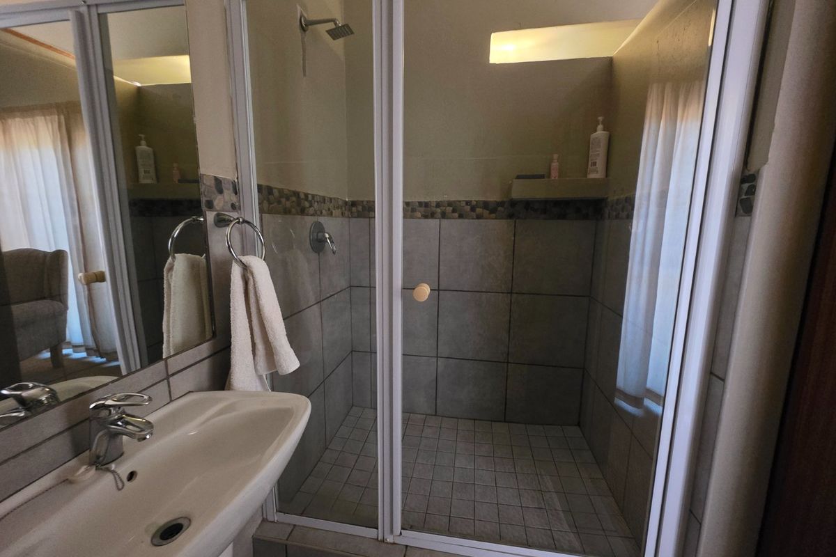 A functional bathroom featuring a pedestal basin, a glass-enclosed shower with tiled walls, and a wall-mounted mirror.