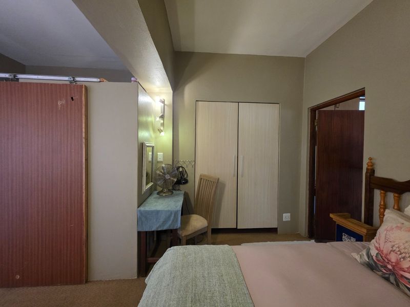 A bedroom featuring a built-in wardrobe, neutral wall tones, and a sliding door entrance, offering a functional layout with potential for cosmetic updates.