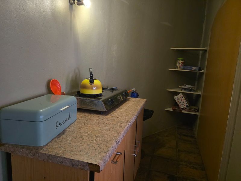 A compact kitchen area featuring laminate countertops, base cabinetry, and corner shelving, requiring cosmetic updates to the wall finishes.