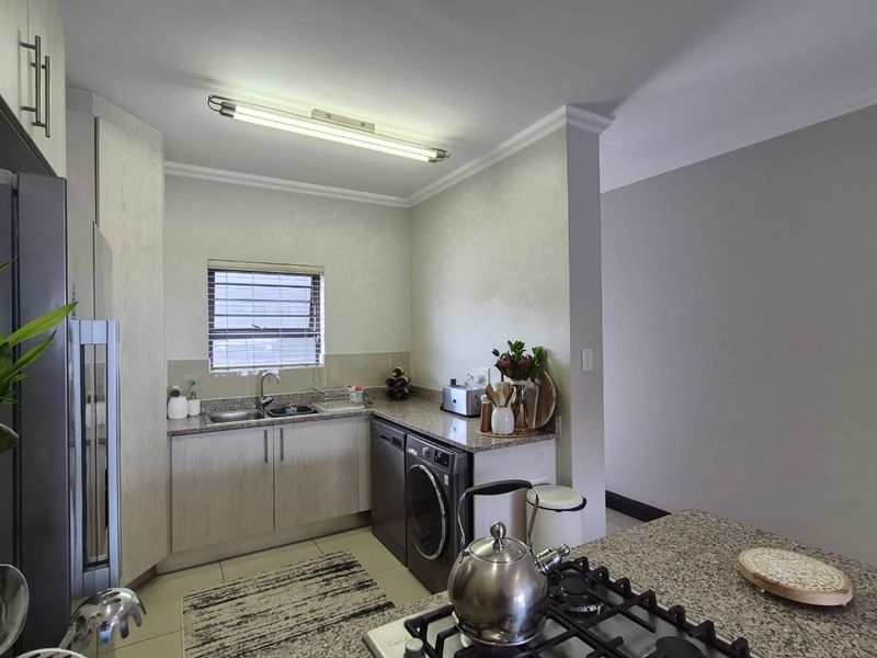 A functional kitchen featuring granite countertops, built-in cabinetry, a gas hob, and an integrated washing machine, offering a clean and practical workspace.