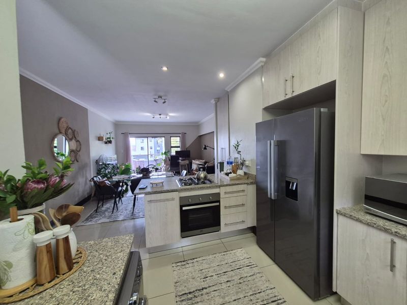 Open-plan kitchen and living area featuring modern cabinetry, granite countertops, integrated appliances, and tiled flooring leading to a balcony.