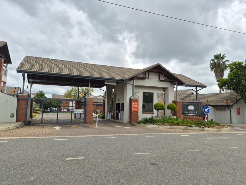 The secure entrance gate and guard house of Edward Place apartment complex, featuring brick pillars, tiled roofing, and paved visitor access.