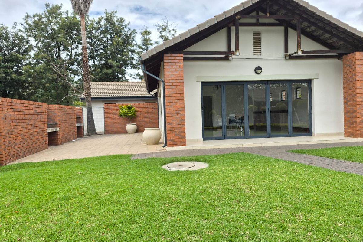 Rear view of the property featuring a paved patio area with a built-in brick braai and modern folding glass doors leading into the home.