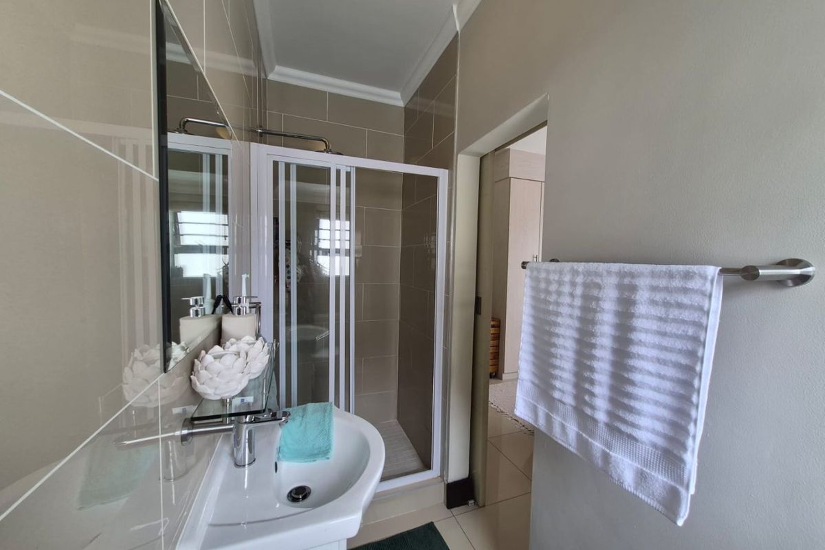 A clean, modern bathroom featuring a pedestal basin, a glass-enclosed shower, and neutral ceramic tiling throughout.