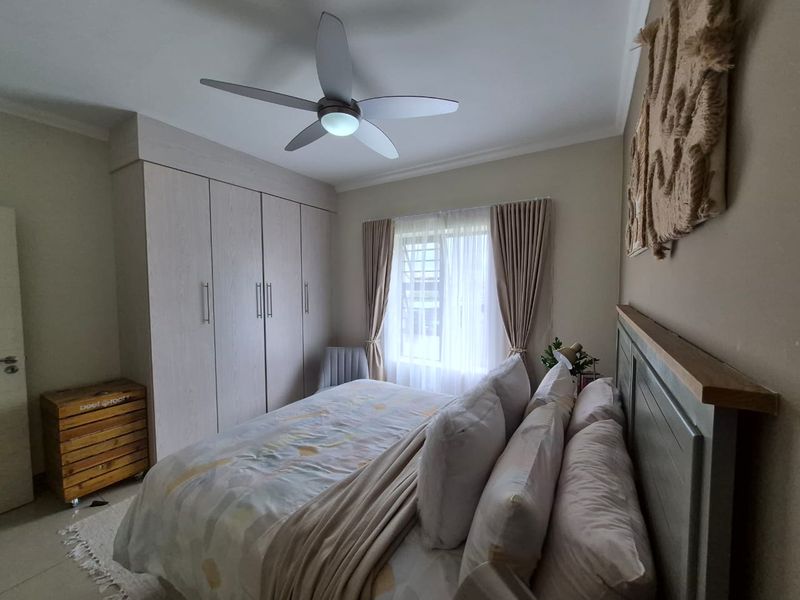 A well-maintained bedroom featuring built-in cupboards, a modern ceiling fan, and neutral finishes, providing a comfortable and functional living space.