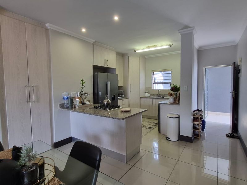 Modern open-plan kitchen featuring granite countertops, light wood cabinetry, gas hob, and sleek tiled flooring, seamlessly flowing into the living area.