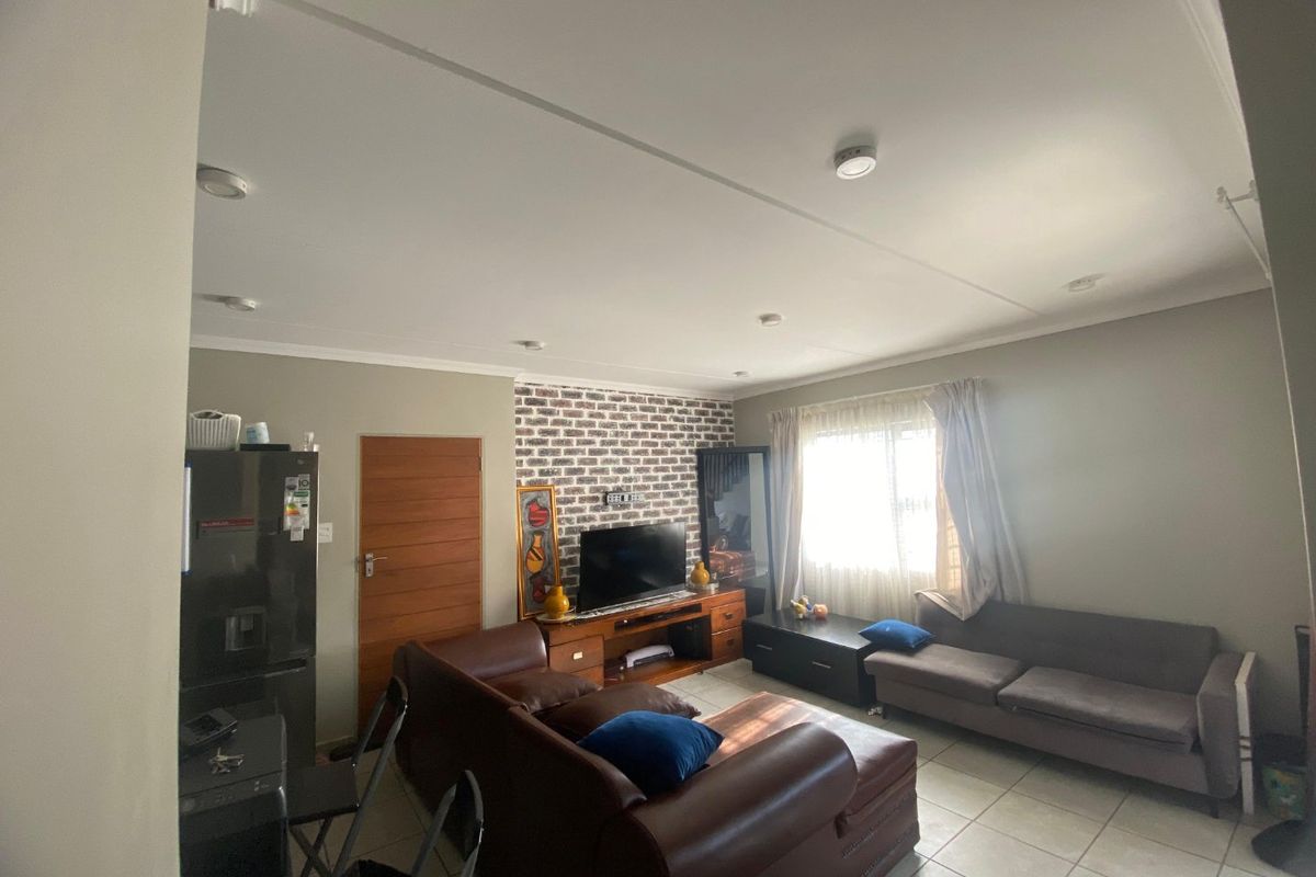A living room featuring an exposed brick accent wall, tiled flooring, and recessed ceiling lighting, providing a functional and comfortable living space.