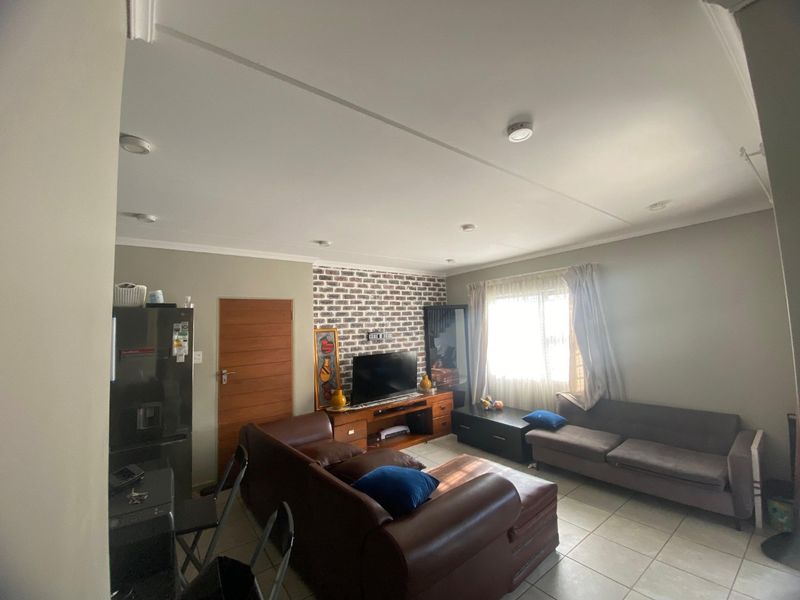 A living room featuring an exposed brick accent wall, tiled flooring, and recessed ceiling lighting, providing a functional and comfortable living space.