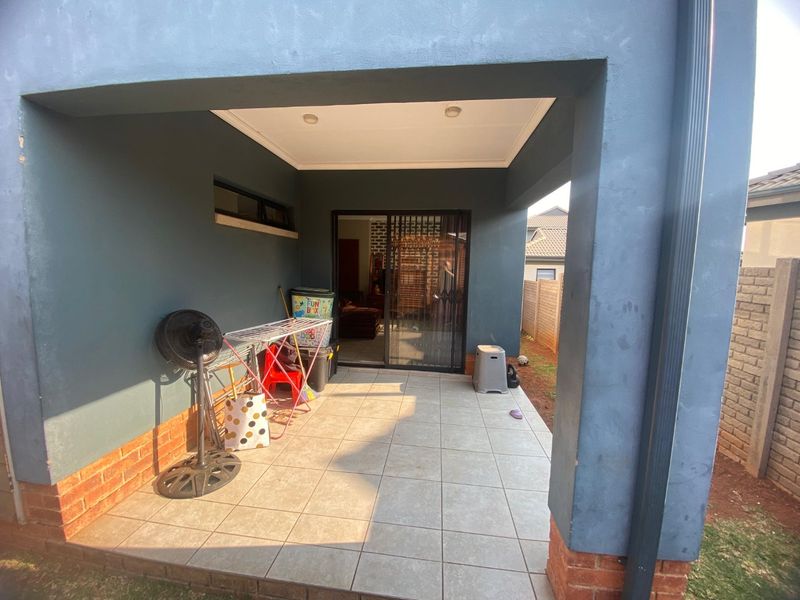A covered patio area featuring tiled flooring, recessed lighting, and a sliding glass door with a security gate, providing access to the interior.