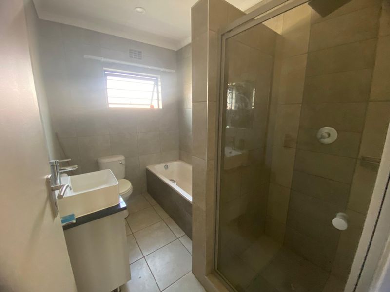 A functional bathroom featuring a built-in bathtub, separate glass-enclosed shower, vanity basin, and toilet with neutral tiled finishes.