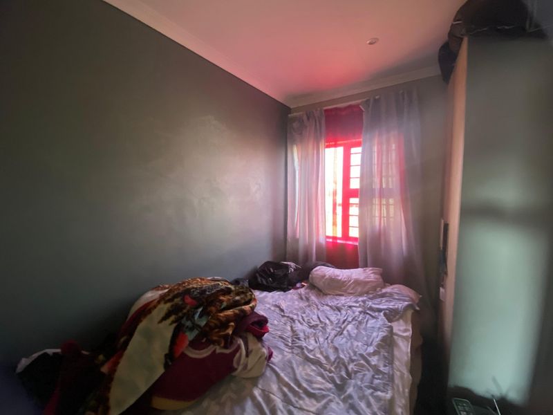 A compact bedroom featuring a built-in wardrobe and a window fitted with security bars, providing a functional sleeping space.