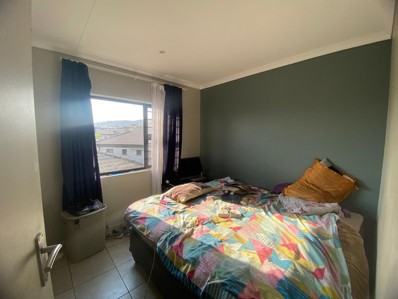 A bedroom featuring tiled flooring, a coved ceiling, and an aluminium window frame with views of the surrounding neighbourhood.