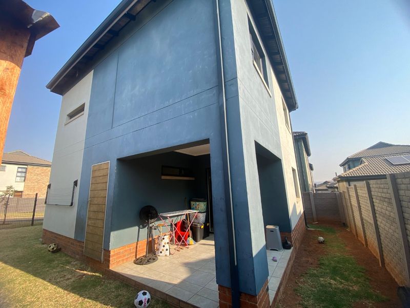 Rear view of a two-story house featuring a covered tiled patio area, blue and white exterior paint, and a surrounding garden with boundary walling.