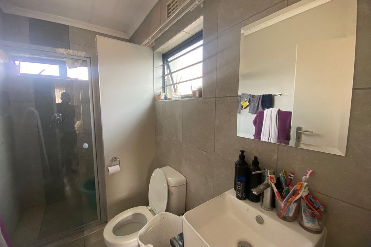 A functional bathroom featuring a shower enclosure, toilet, and a modern basin with a wall-mounted mirror and tiled finishes throughout.