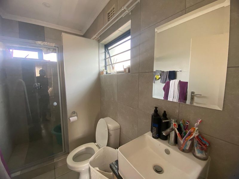 A functional bathroom featuring a shower enclosure, toilet, and a modern basin with a wall-mounted mirror and tiled finishes throughout.