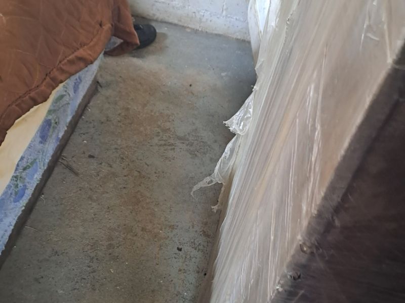 A bedroom space featuring exposed brick walls and unfinished concrete flooring, requiring significant renovation and finishing to reach a habitable standard.