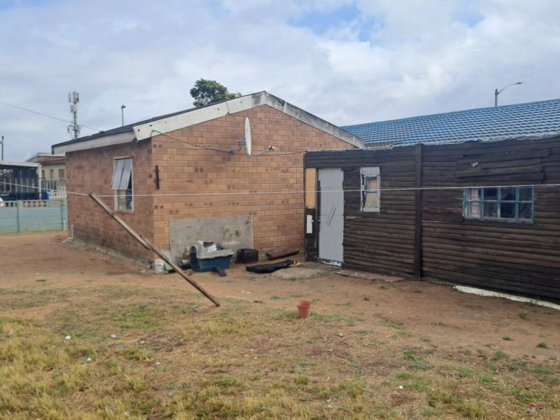Rear view of the property showing a combination of brick and timber-clad structures with visible signs of wear and maintenance requirements.