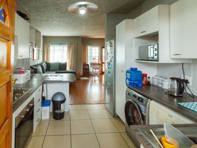 Open-plan kitchen and living area featuring tiled flooring, built-in cabinetry, and integrated laundry facilities, offering a functional layout for modern apartment living.