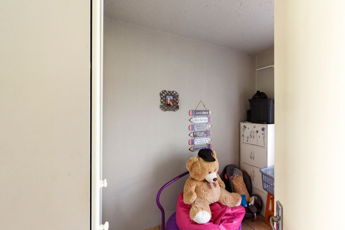 A compact bedroom space featuring neutral wall finishes and tiled flooring, viewed through an open doorway.