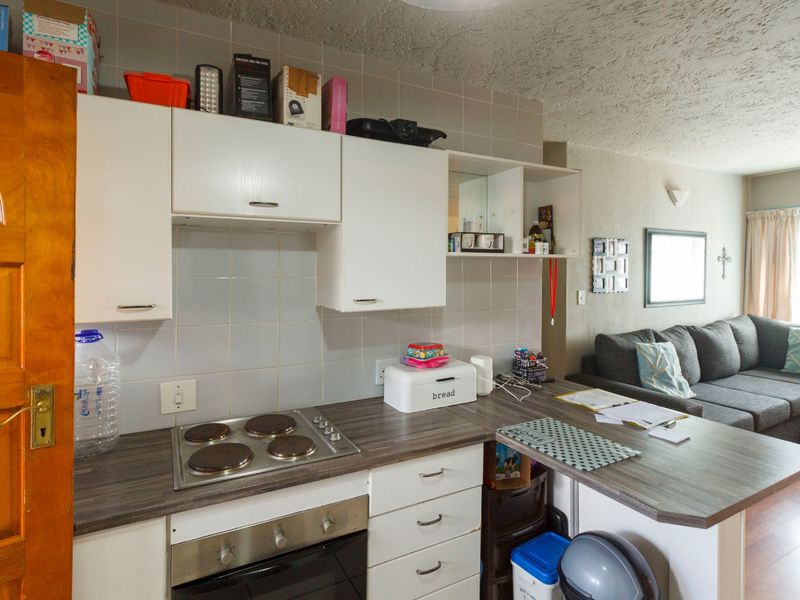 Open-plan kitchen featuring a compact layout with an electric hob, built-in oven, laminate countertops, and white cabinetry, seamlessly flowing into the living area.