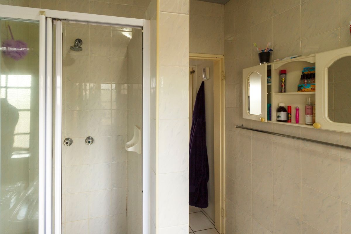 A dated bathroom featuring a shower enclosure with tiled walls and a built-in wall cabinet, offering potential for modernization.