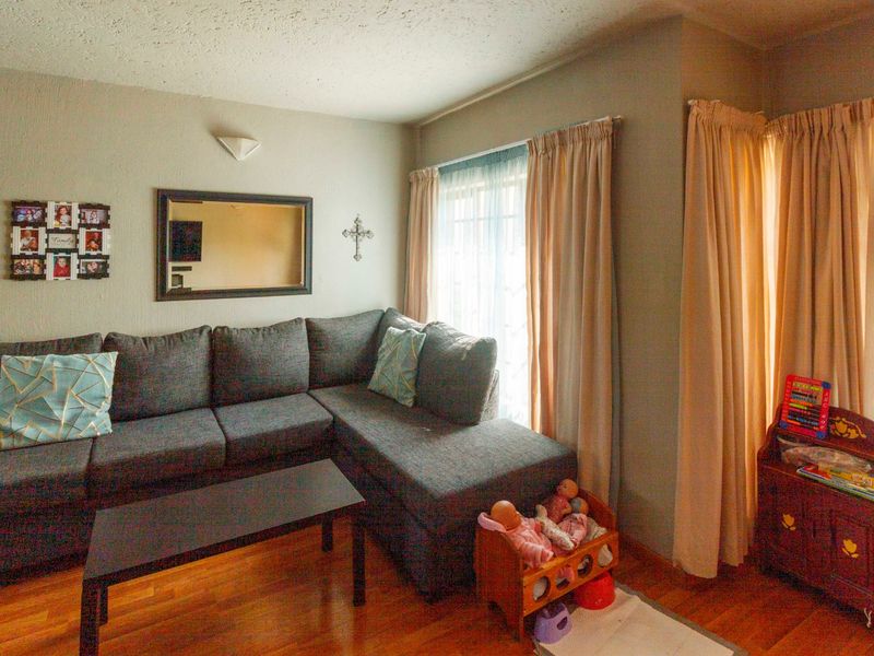 A cozy living room featuring laminate flooring and natural light provided by large windows with curtain tracks.