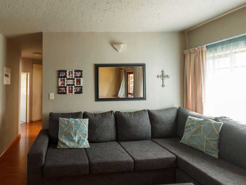 A comfortable living room featuring laminate flooring, a wall-mounted light fixture, and natural light from the window.