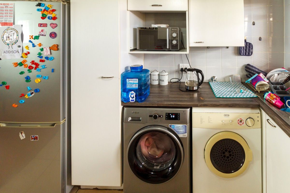 A functional kitchen area featuring built-in cabinetry, a laminate countertop, tiled backsplash, and dedicated space for laundry appliances.