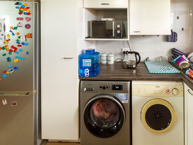 A functional kitchen area featuring built-in cabinetry, a laminate countertop, tiled backsplash, and dedicated space for laundry appliances.