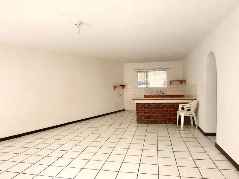 An empty open-plan living and kitchen area featuring tiled flooring, a brick breakfast bar, and a classic arched doorway.