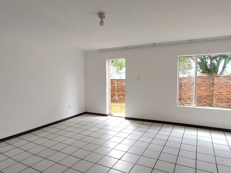 An empty, open-plan living area featuring white walls, ceramic tiled flooring, and direct access to an outdoor space through a security door.