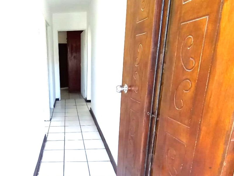 A narrow hallway featuring white walls, tiled flooring, and a traditional wooden door with decorative detailing.
