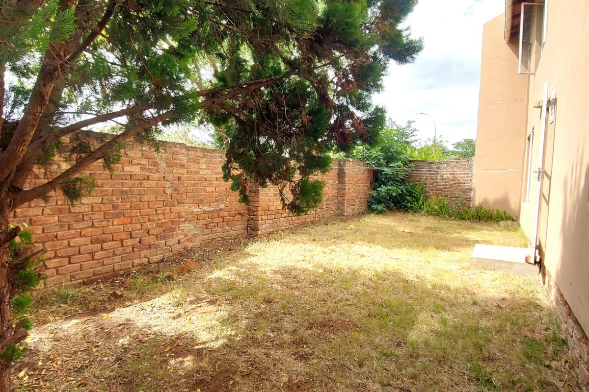 A private rear garden area featuring an exposed brick boundary wall and established trees, adjacent to the main building structure.