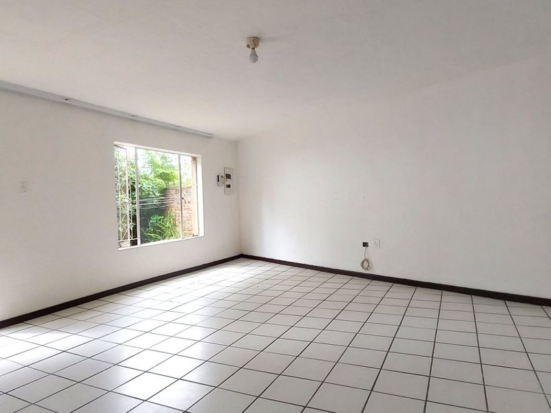 A spacious, empty living area featuring white walls, tiled flooring, and direct access to an outdoor space through a doorway.