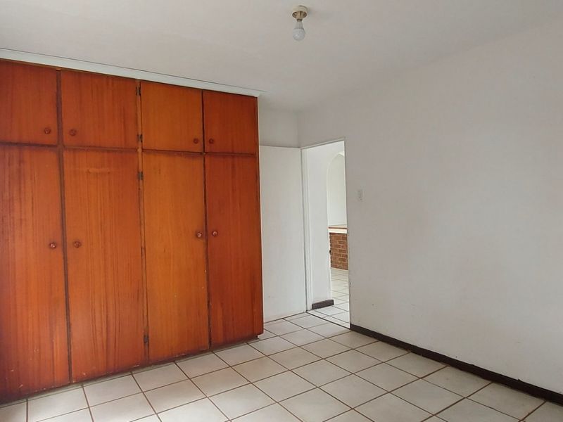 A vacant bedroom featuring tiled flooring and floor-to-ceiling built-in wooden cupboards, offering a blank canvas for renovation or restyling.