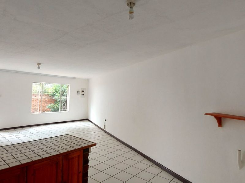 An empty open-plan living and kitchen area featuring tiled flooring, a built-in counter, and direct access to an outdoor space.