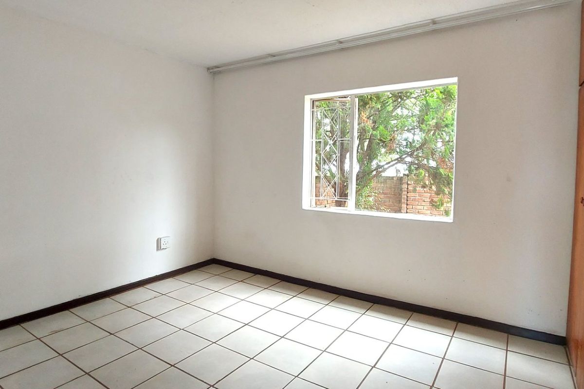 A vacant bedroom featuring tiled flooring, built-in wooden cupboards, and a window with security bars, offering a blank canvas for personalization.