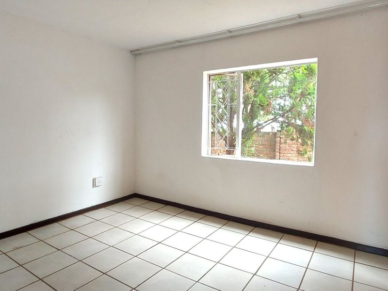 A vacant bedroom featuring tiled flooring, built-in wooden cupboards, and a window with security bars, offering a blank canvas for personalization.