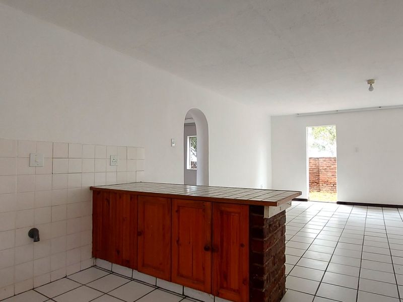 Spacious open-plan living and kitchen area featuring tiled flooring, a breakfast counter with brick base, and direct access to the exterior.